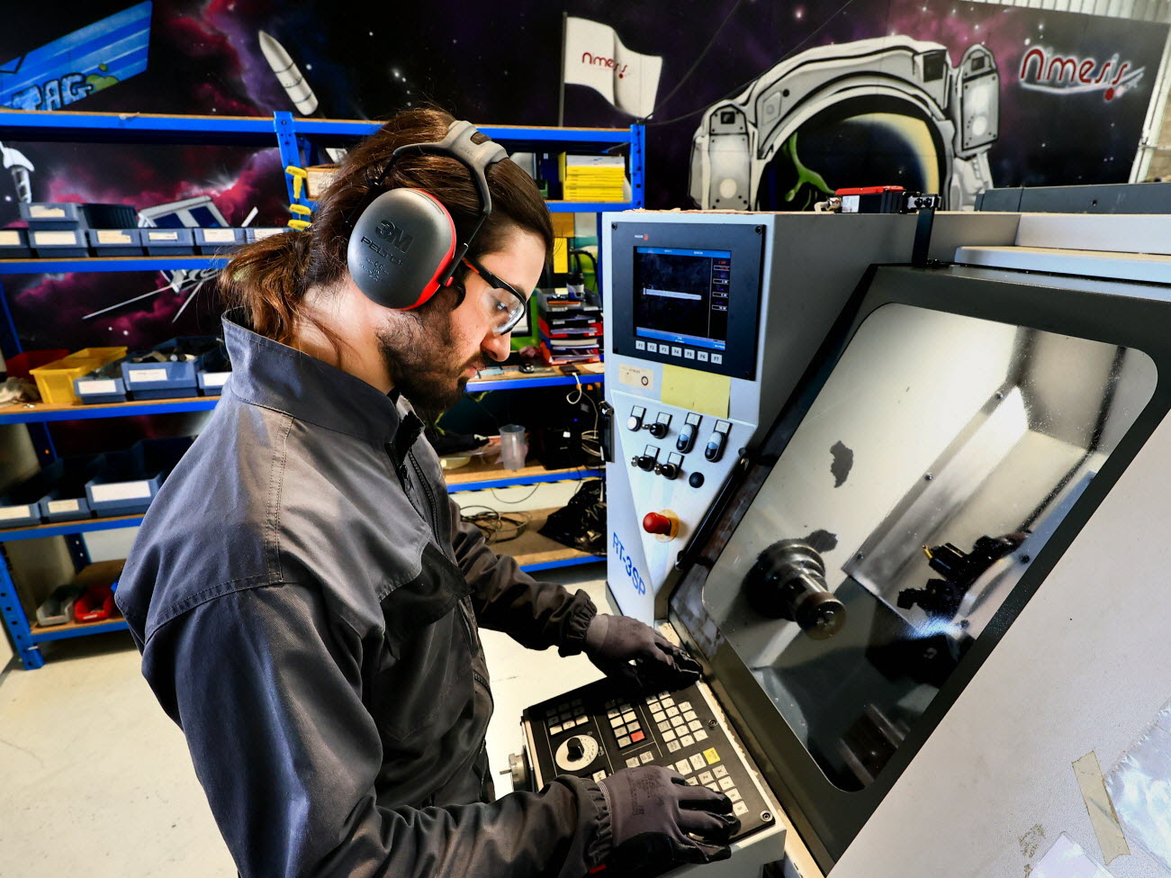 Technicien Nimesis utilisant une machine pour la fabrication de composants de haute précision dans un atelier industriel.